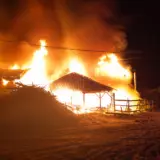 A large house engulfed in intense orange flames and thick smoke at night during a structural fire